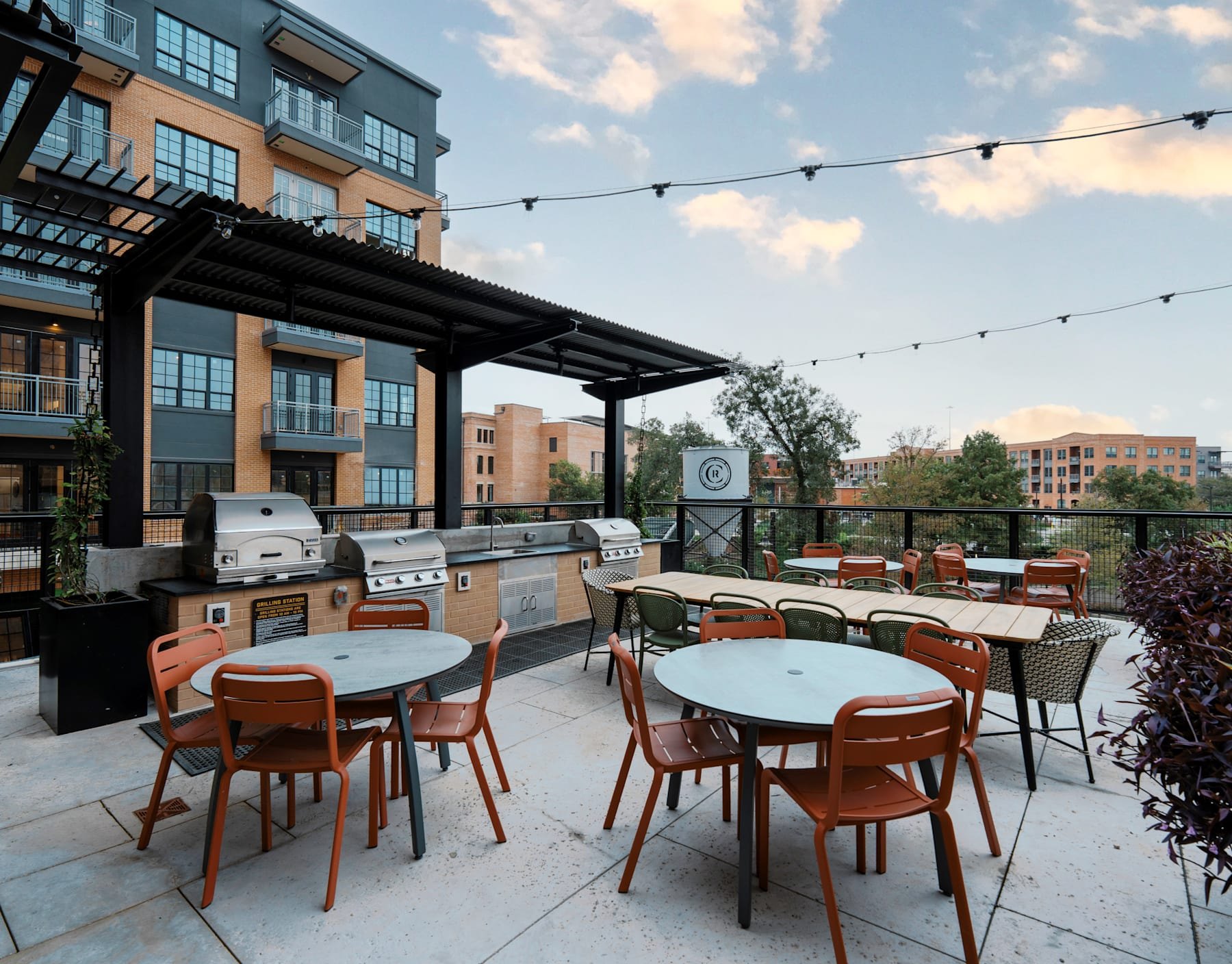 Outdoor terrace with orange chairs, grills, and string lights