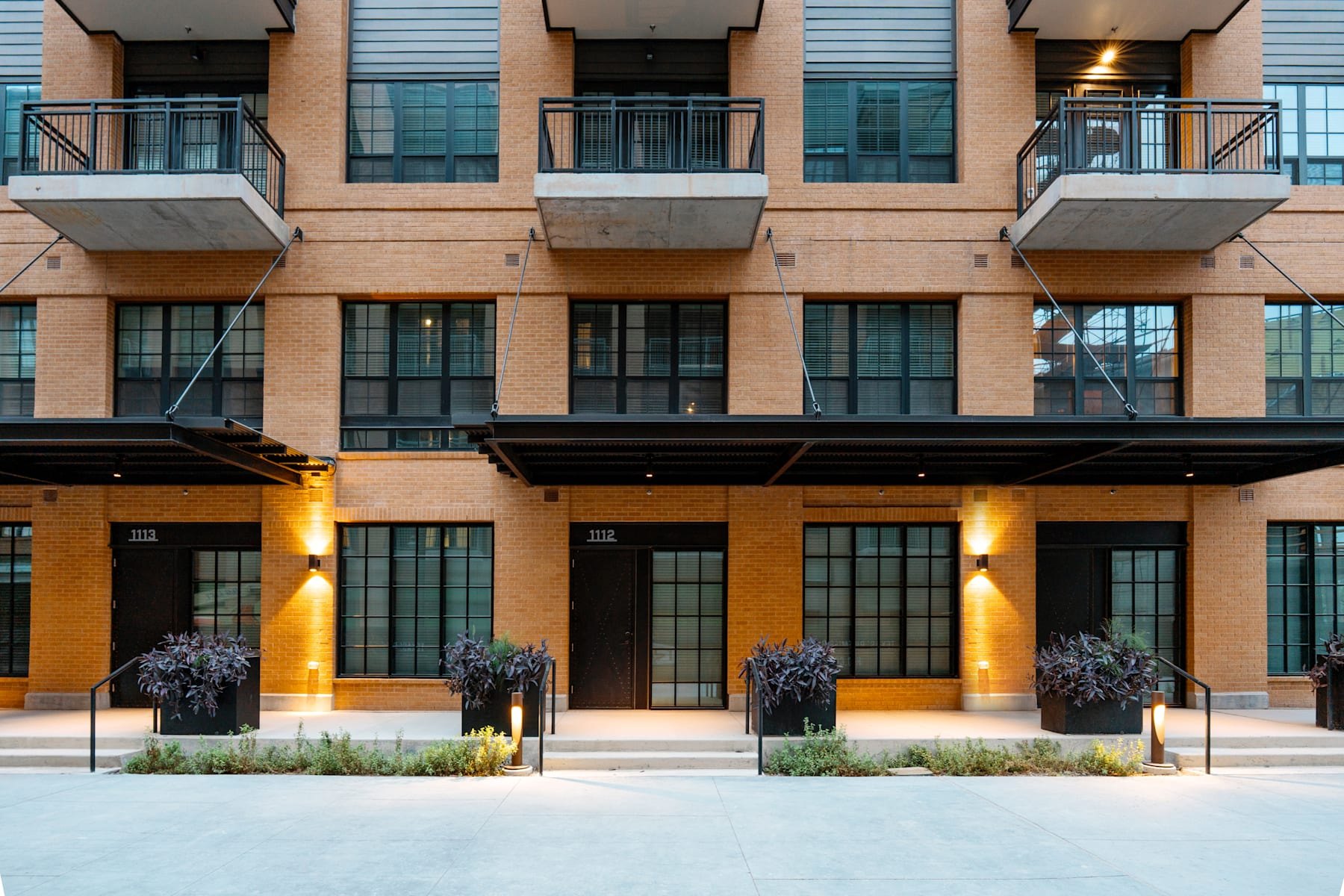 Brick residential facade with black awnings, balconies, and unit doors